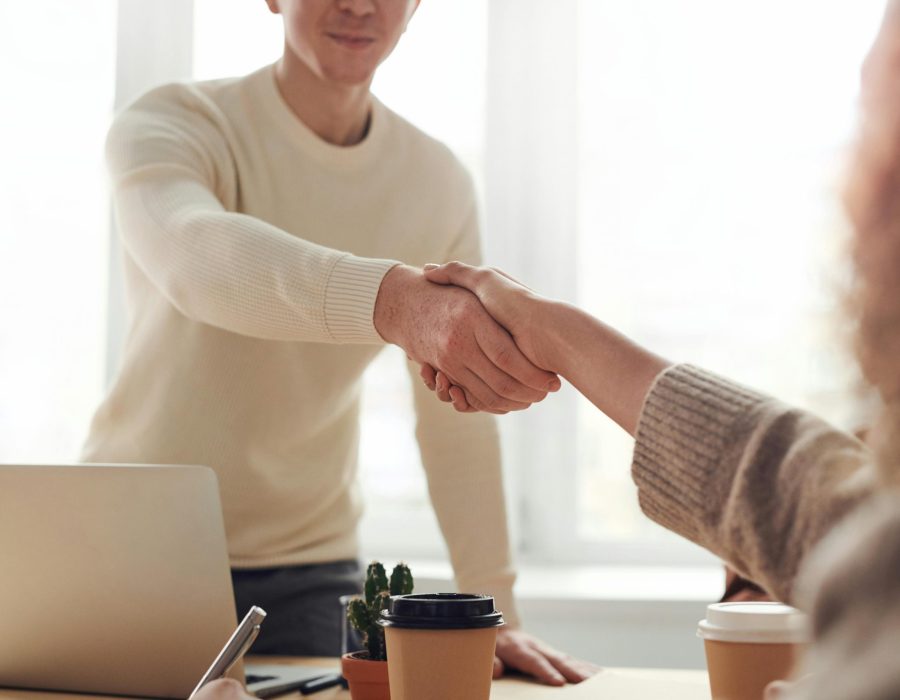 Close-up of professionals shaking hands over coffee in a modern office.